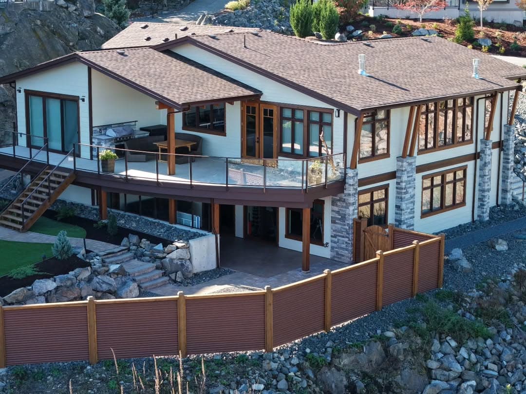 Custom home with timber beams, stone pillars, and siding — drone view